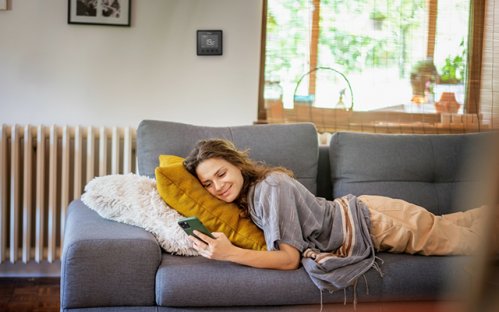 Une femme couchée dans un canapée. Elle profite de l'ambiance agréable grâce au thermostat connecté